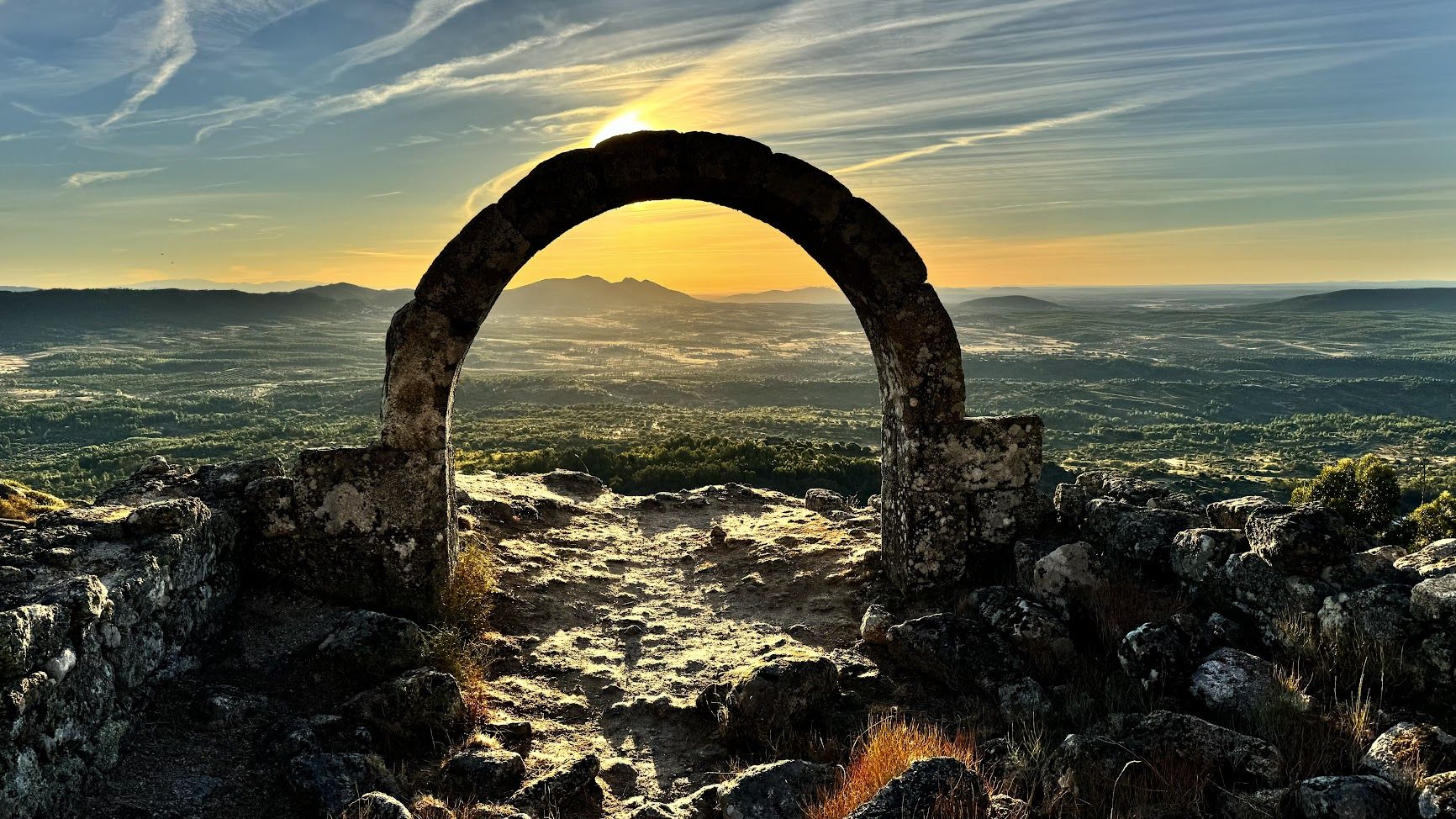 A stone arch on a hilltop at sunset